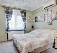 Bedroom in a 2-room apartment with a bed, paintings, and air conditioning on the wall.