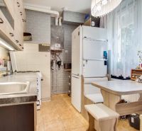 A kitchen in a 2-room apartment with appliances, a dining area, and a decorative brick wall.
