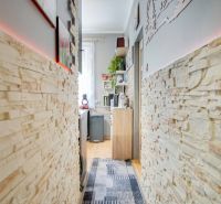 A narrow corridor with light brick cladding leading to the kitchen in a 2-room apartment.