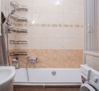 Bathroom with a bathtub and a washing machine in a 2-room apartment. Tiles with a beige decor.