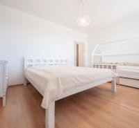 A bedroom with wood-patterned flooring, a double bed, and a child's bed.