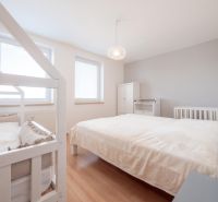 A bright bedroom in a two-room apartment with a bed, a baby crib, and a wooden decor floor.