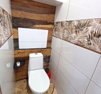 A bathroom in a holiday apartment with decorative tiles and a wooden-patterned floor.