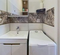 Bathroom in a holiday apartment with a washing machine and patterned wall tiles.