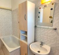 A bathroom with a bathtub and a sink in a studio apartment.