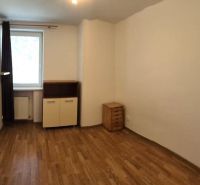 A room of a one-room apartment with a wooden decor floor, furniture, and white walls.