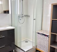 Bathroom with a shower, cabinet, and laundry basket in a 2-room apartment.