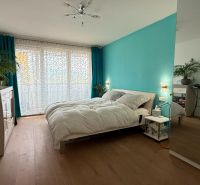 A bright bedroom with a turquoise wall, wood-patterned flooring, and a mirrored wardrobe in a four-room apartment.