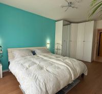 A bright bedroom with a turquoise wall, white wardrobes, and a wood-patterned floor.