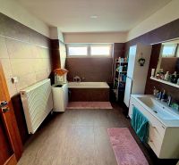 A bathroom in a family house with a bathtub, cabinets, a washing machine, and a floor with a wooden decor.