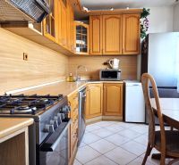 A kitchen in a 3-room apartment with wooden cabinets, a gas stove, and a dining table.
