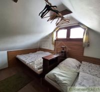 Attic with two beds, wooden decor floor, hangers, small window, low ceiling.