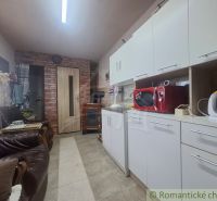 A kitchen in a cottage with white cabinets, a red microwave, and leather sofas.