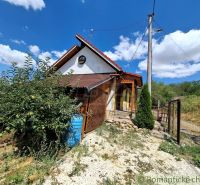 A cottage in Gbelce surrounded by greenery and trees under a blue sky.