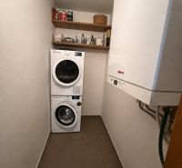 Laundry room in a 3-room apartment with a washing machine, dryer, shelves, and a gas boiler.