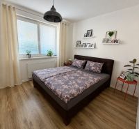A bedroom with a bed, wooden decor flooring, and decorations in a three-room apartment.