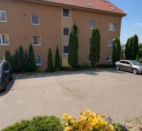 Parking lot in front of the apartment building in Veľký Lapáš with cars and greenery around.