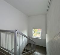 A staircase with a window in a 2-room apartment, the walls are white with a metal railing.