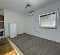A kitchen in a 2-room apartment with a wooden decor floor, a white refrigerator, and a stove.