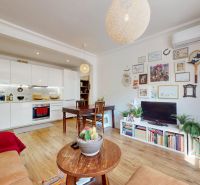 Living room of a three-room apartment with an open kitchen and a wooden decor floor.