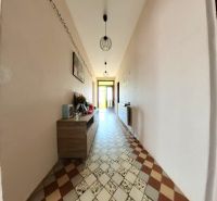 A hallway of a family house with a tiled floor, a chest of drawers, and ceiling lamps.