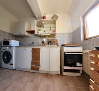 A kitchen in a family house with a ceramic floor, cabinets, a stove, a microwave, and a washing machine.