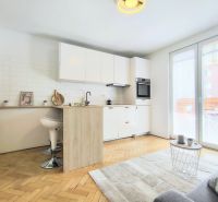 A kitchen in a 2-room apartment with white furniture, a floor with a wooden decor.