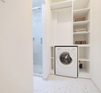 Bathroom with a shower and a washing machine in a 2-room apartment. White shelves increase storage options.