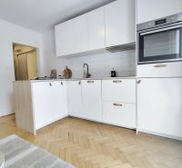 A kitchen in a 2-room apartment with light cabinets and a wooden decor floor.