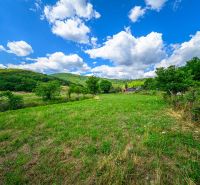 A plot of land surrounded by greenery near Hajnáčka with a clear blue sky and white clouds.