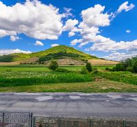 The landscape near a family house in Hajnáčka, meadows and hills under a blue sky.