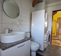 A bathroom in a 2-room apartment with a sink, a round mirror, and a washing machine.