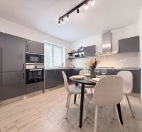 A kitchen with dark cabinets and a dining table in a two-room apartment with a wooden decor floor.