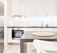 A kitchen in a 2-room apartment with white cabinets and a stainless steel refrigerator.