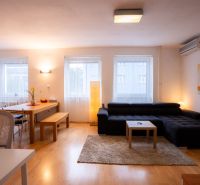 Living room of a 4-room apartment with a sofa, dining table, and wooden decor flooring.