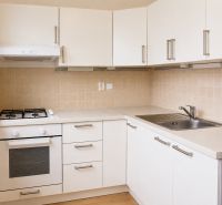 A kitchen with white cabinets and appliances in a 2-room apartment, floor with wood decor.