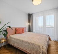 A bright bedroom with a bed, a plant, and a wooden decor floor in a 3-room apartment.