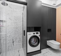A bathroom with a washing machine and shower in a 3-room apartment decorated with marble tiles.
