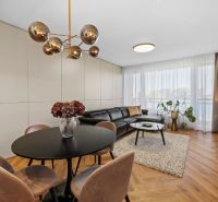 A living room in a three-room apartment with a wooden decor floor, a large window, and elegant lighting.