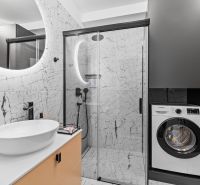 A bathroom in a 3-room apartment with marble tiles, a washing machine, and a shower.
