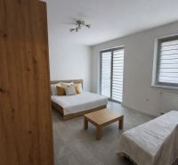 A room with a bed, a table, and a floor with a wooden decor in a studio apartment.