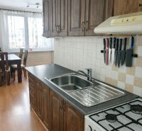 A kitchen in a 3-room apartment with a wooden decor floor and stylish cabinets.