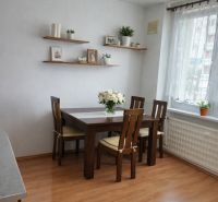 Dining area with a table, chairs, and shelves on a wooden floor in a 3-room apartment.