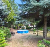 A garden in Mankovce with a swimming pool and a bench in the shade of trees near a family house.