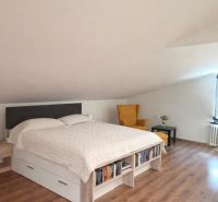 Bedroom in a family house with a wood-patterned floor, a bed, and a chair.