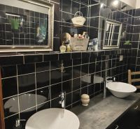 A bathroom in a family house with black tiles, two sinks, and mirrors.
