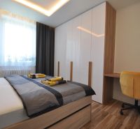 A bedroom in a 3-room apartment with a bed, wardrobe, yellow armchair, and a floor with a wooden decor.