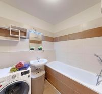 A bathroom in a 3-room apartment with a bathtub, washing machine, and modern tiling.
