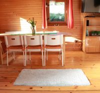 A wooden interior of a cottage with a dining table, white chairs, and a floor with a wooden decor.
