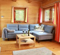Living room of a cottage with wooden walls, a wooden-patterned floor, a blue sofa, and a table.